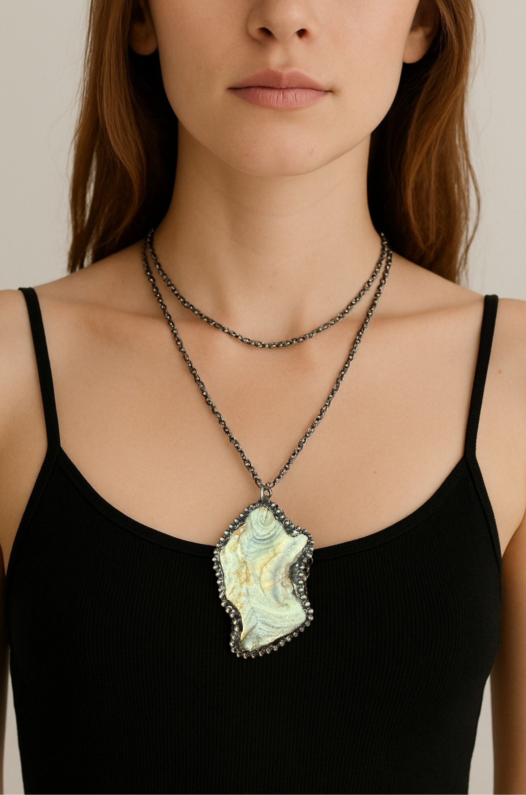 Woman wearing a black top with a necklace featuring a large, decorative pendant.